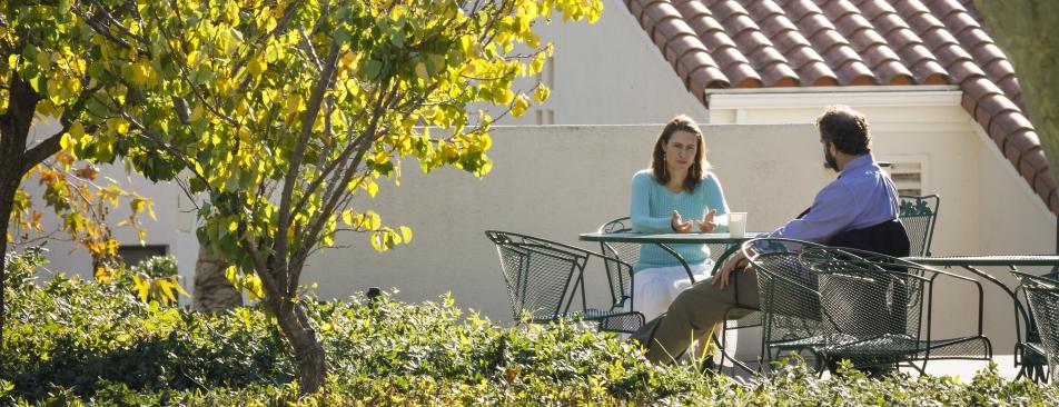 两个人坐在外面一棵树旁的一张桌子旁